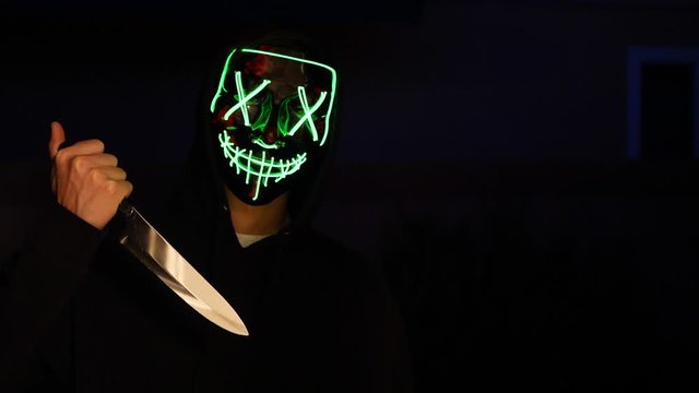 A creepy slasher killer in a generic anonymous halloween horror mask pulling a knife on his murder victim.