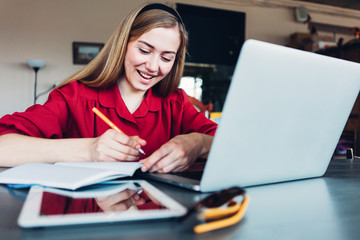 Smiling focused woman sitting with laptop and tablet in big bright open space. Wearing red...