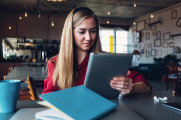 Fototapeta premium Young woman in red suit reading tablet computer in big open space. Paperwork and cup of coffee on the table