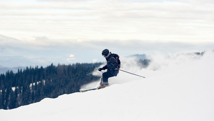 Side view of freerider skier descending from mountain in deep white snow powder. Popular kind of winter sport. Skier on slope. Concept of extreme amateur sport. Mountains view. Grey sky on background.