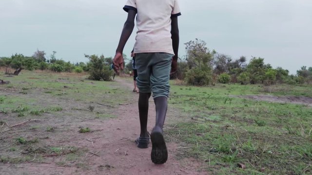 African child walking in refugee settlement to water source.