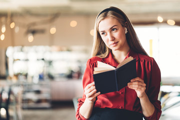 Pretty smiling woman reading book near in big bright open space, wearing red smart-casual dress