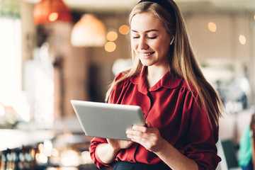 Pretty woman with tablet computer in hands, wearing red dress and standing in open space