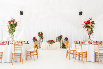 Beautiful banquet hall under a tent for a wedding reception. Interior of a wedding tent decoration ready for guests. Decor flowers. Red theme