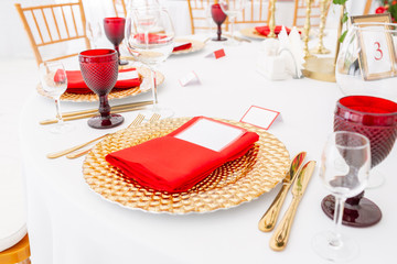 Table setting red napkins and glasses, gold plates. Interior of a wedding tent decoration ready for guests. Decor flowers. Red theme