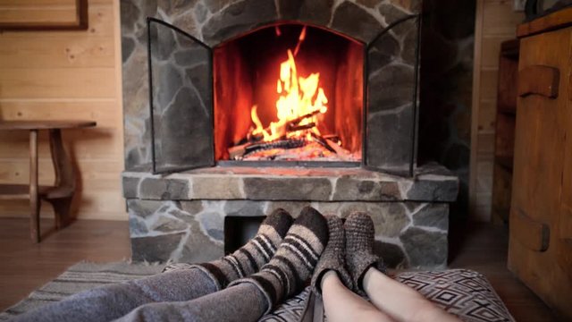 Couple in wool socks warming by cozy fire. Romantic winter evening