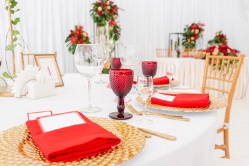 Table setting red napkins and glasses, gold plates. Interior of a wedding tent decoration ready for guests. Decor flowers. Red theme