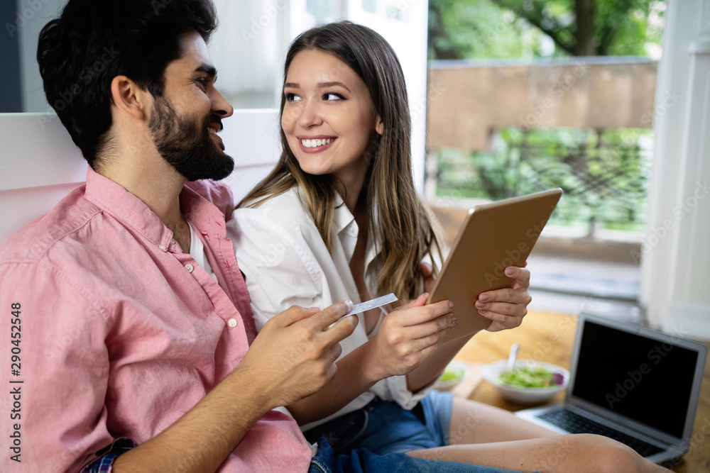 Wall mural young happy couple sitting on the floor with laptop booking holidays