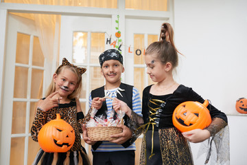 Portrait of children dressed in costumes holding basket with sweets and lanterns and smiling at...