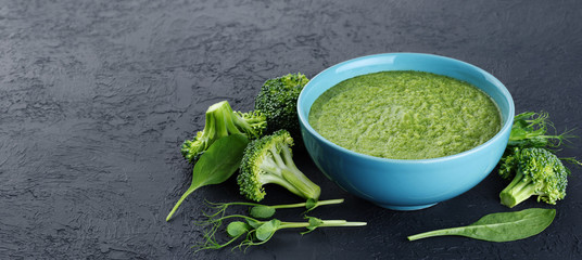 Bowl of green cream soup with pea sprouts, broccoli, kale and spinach on a dark background.