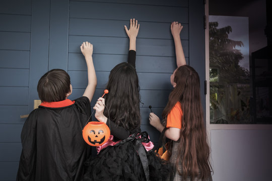 Group of girl and boy kids smiling and dress up as Halloween vampire costume and knock on door for trick or treat for Halloween night day theme coming soon together, back view