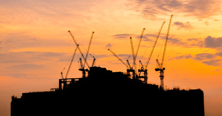 Silhouette building under construction with crane over sunset background