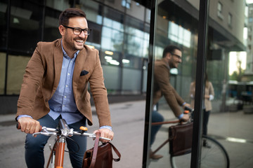 Happy young stylish businessman going to work by bike