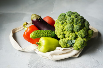 Set of products in a cotton eco bag on a marble table, eggplant, broccoli, tomatoes, peppers, zucchini. The concept of zero waste.