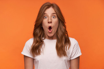 Close-up portrait of shocked curly female in white t-shirt posing over orange background with...