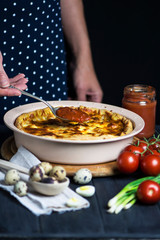 chef's hand cook tasty meat pie with carrots, onions and cheese in a baking dish on a dark background