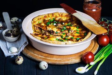meat pie with carrots, onions and cheese in a baking dish on a dark background