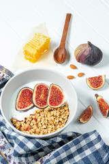 white wheat granola with low-fat yogurt in a white bowl in a composition with a spoon, honeycombs and fig on white wooden background. Healthy breakfast food. Making breakfast. Gluten free