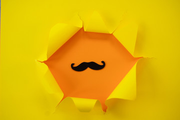ripped yellow paper against a orange background with mustache in it