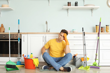 Tired young man sitting on floor after cleaning kitchen