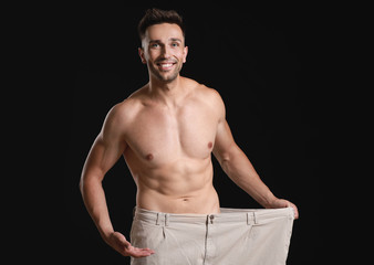 Fototapeta na wymiar Handsome muscular man in loose pants on dark background. Weight loss concept
