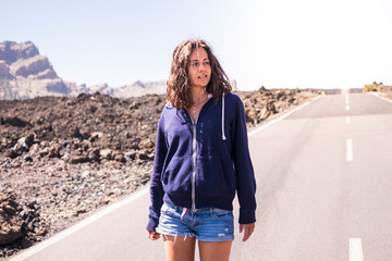 Beautiful young model with shorts standing on a long way asphalt road and bright sky in backgorund - concept of travel and outdoor eisure activity