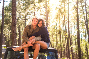Cheerful happy people young couple sit down on the roof of the off road car enjoying the nature during travel excursion in the forest - concept of adventure and alternative vacation