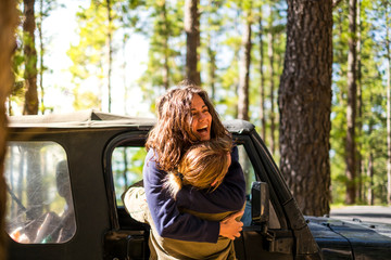 Happy beautiful young woman hugged with love by boyfriend outside the car used to travel - natural forest in background concept of relationship and together forever people