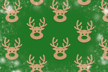 Wooden Christmas toys head of a deer is lined with a pattern on a green background with the effect of falling snow. Merry Christmas and Happy New Year concept. Minimalistic style. Flat lay, top view