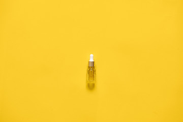Glass bottle with dropper with serum or essenatial oil. Yellow background, natural medicane concept