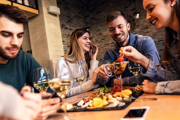 Group of young friends having fun in restaurant, talking and laughing while dining at table.