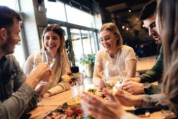 Group of young friends having fun in restaurant, talking and laughing while dining at table.