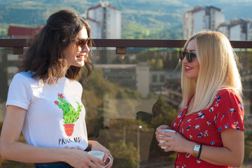 Two female friends drinking coffee at balcony. 