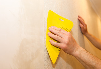 Man is using scraper to install wallpaper. Levelling of the wall. Maintenance repair works renovation in the flat. Restoration indoors.