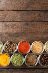 Colourful seasonings in bowls on wooden background with copyspace. Collection of spices