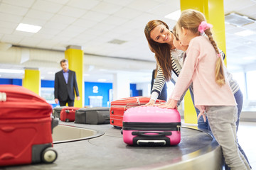 Mutter und Kinder suchen ihre Koffer am Gepäckband