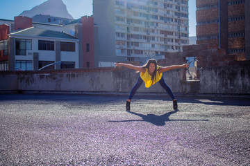 Beautiful woman in jeans and a yellow top dancing on a rooftop.