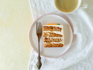 A slice of carrot cake on a round plate and a Cup of coffee on a light background top view.