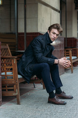 portrait of an attractive young man in a blue suit in the city on gray background.watch on hand, gold wrist watch.pensive