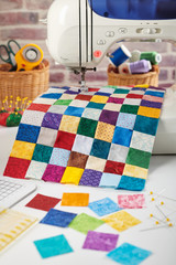 Colorful detail of quilt sewn from square pieces on sewing machine, quilting and sewing accessories