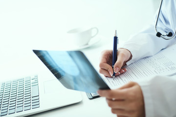 Fototapeta premium Close up of female doctor holding x-ray or roentgen image and making notes in medical form.