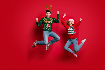 Fototapeta na wymiar Full size photo of funky lady and guy jumping excited by x-mas prices wear ugly ornament jumpers and headwear isolated red color background