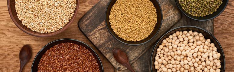 panoramic shot of bowls with buckwheat, chickpea and beans near spoons on wooden cutting boards