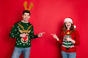 Photo of funny lady and guy directing fingers empty space advising good choice wear knitted ugly...