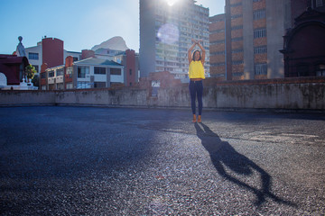 Beautiful woman in jeans and a yellow top dancing like a ballerina on a rooftop.