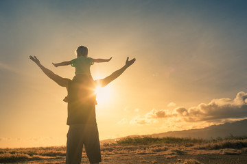 Father son having fun outdoors at sunset pretending to fly. Family adventure and freedom concept.