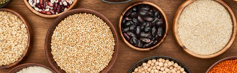 panoramic shot of bowls with oatmeal, buckwheat, quinoa, beans and chickpea on wooden surface
