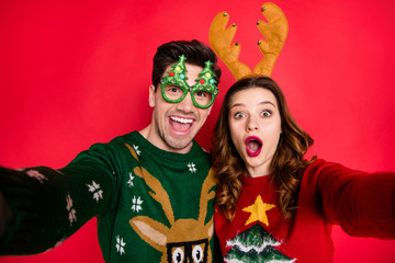Photo of excited lady and guy chilling at newyear costume party making selfies wear funky pullovers with ugly ornaments isolated red color background