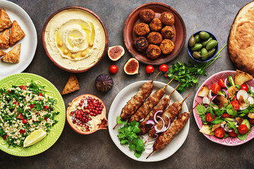 Arabic and Middle Eastern dinner table. Hummus, tabbouleh salad, Fattoush salad, pita, meat kebab,...