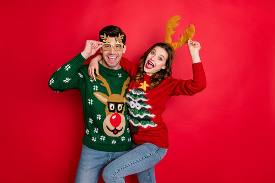 Portrait of crazy two people wife husband student hipster hug embrace wear brown comfort cozy pullover sweater with chritsmas tree design denim jeans eyewear isolated over red color background